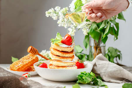 Honey pouring over a stack of mini pancakes with strawberryの写真素材