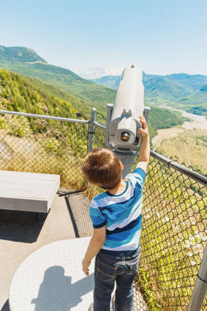 Little boy reaches for telescope to see Mount St. Helens snow capped top, Washington state, USAの写真素材
