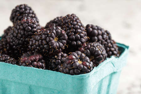 Fresh and ripe blackberries from the farmers market in blue paper box, closeup