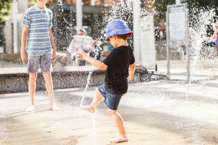 Cute little boy playing with water jet in fountain on a heat summer day.の写真素材