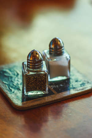 Salt and black pepper in shakers closeup on wooden table