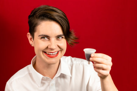Happy woman holding a menstrual cup - an alternative sanitary product to collect menstrual blood inside, red background, focus on eyesの写真素材