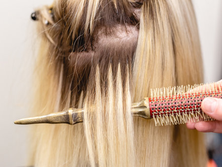 Hair extensions correction procedure. Hairdresser does hair extensions to blonde hair lady in a beauty salonの写真素材