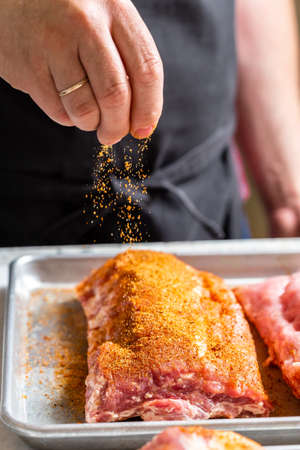 Preparing meat for barbecue grilling. Raw St Louis Style BBQ Ribs covering with salt and spicesの写真素材