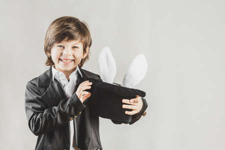 Adorable child dressed as an illusionist getting bunny from a hat over grey backgroundの写真素材