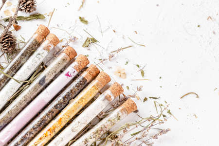 Variety of bath salts in glass tubes with dry herbs around. Natural organic SPA cosmetic product. Skin care, beauty treatment concept, space for textの写真素材
