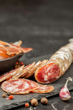 Traditional smoke dried pork sausage on a slate board and jerky ham stack with spices and garlic. Space for textの写真素材