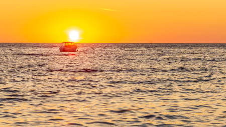 Single fishing boat in the middle of the sea at sunsetの写真素材