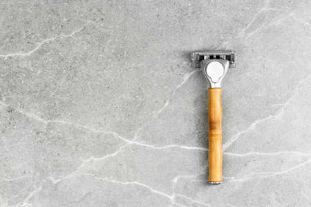 Shaving Razor with wooden handle on a grey marble background. Plastic free hygiene tool. Free space for brandingの写真素材