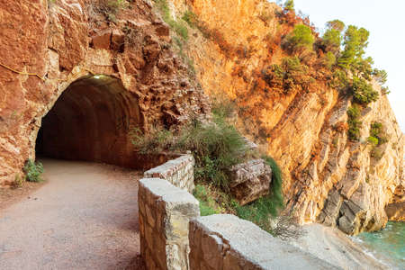 The entrance to Crvena Stijena Tunnel cut out in the seaside rocky cliffs on the walking path in Petrovac bay in Montenegroの写真素材