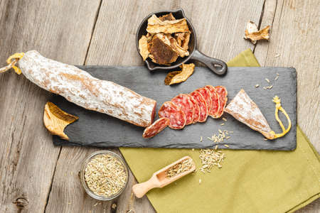Above photo of Sliced Salami Sausage with Dried Slices of Porcini Mushrooms and Fennel Herb on wooden background.の写真素材
