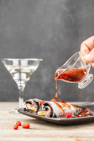 Pouring strawberry jam on thin crepes rolls. Brown pancakes rolls poured berry jam and decorated fresh strawberries.の写真素材