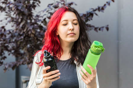 Woman is choosing between two types of reusable water bottles. Aluminium and silicone water bottle for everyday drinking habit. Sustainable lifestyle conceptの写真素材