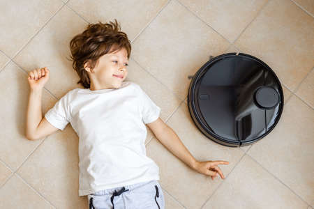 Kid playing with Robotic Vacuum Cleaner. Boy lying on the floor in the way of the Vacuum Cleaner routeの写真素材
