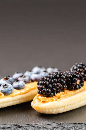 Healthy appetizers with sliced bananas with peanut butter spread, blueberries and blackberries on the top on the slate plate, space for textの写真素材