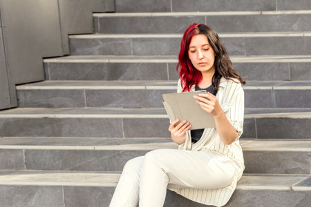 Successful Business woman Using Digital Tablet outhdoors Sitting on the Stairs near the Office Buildingの写真素材