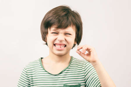 Kid is not happy to have his baby toth fall off. Displeased boy holding his fell out tooth in handの写真素材