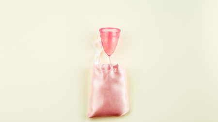 Pink Silicone Menstrual Cup and pink Storage Cloth Bag over beige Background. Space for Text, Top View. Women Sanitary Tool for Comfortable and Sustainable Periodsの写真素材