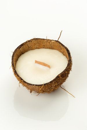 Decorative natural soy wax candle in a coconut shell with wooden candle wick on white glossy surfase. Reuse DIY ideaの写真素材