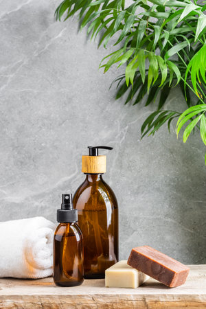 Bathroom table with white towel, dark glass bottles with liquid skin care products and natural handmade solid soap bars over grey marble background and green plant aboveの写真素材