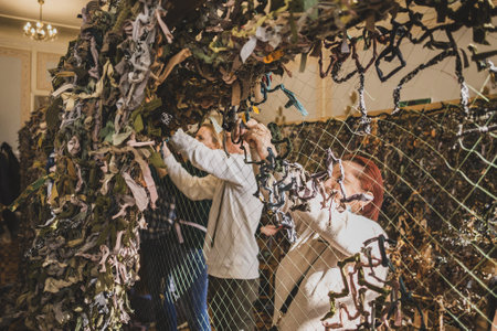 LVIV, UKRAINE - March 17, 2022: Volunteers wawing camouflage net for the Ukrainian military forces. Handmade masking net made of natural colored rugs woven on fishing netのeditorial素材