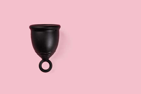 Black menstrual silicone cup on the pink background. Alternative women hygiene product