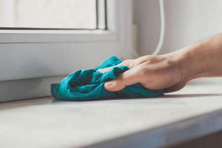 Man cleaning the windowsill with a blue cloth. Doing chores at home