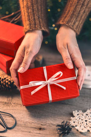 Female hands decorating the red Christmas gift box with the white ribbonの写真素材