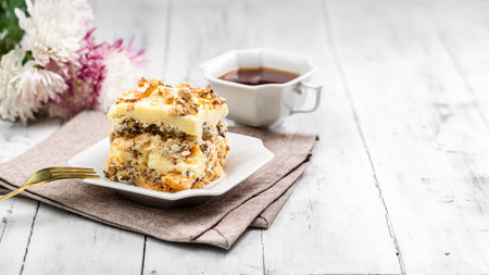 A Piece of Homemade Kyiv Cake or Dacquoise Cake on the White Plate with Cup of Tea and Flowers on the backgroundの写真素材