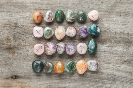 Elder Futhark Rune Stones Set Made of Natural Gemstones on Wooden Backgroundの写真素材