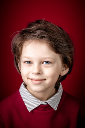 Close up Portrait of Him He Handsome Cute Smiling Smart Caucasian White Boy Dressed in a Red Pullover and Grey Shirt over Dark Red Backgroundの写真素材