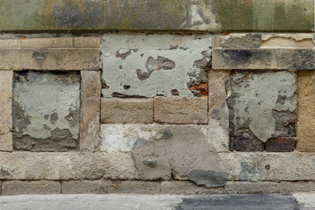 Background Photo of an Old Exterior Wall Built with Sandstone Blocks, Covered with Peeling Plaster. Grunge and Weathered Textured Surfaceの写真素材