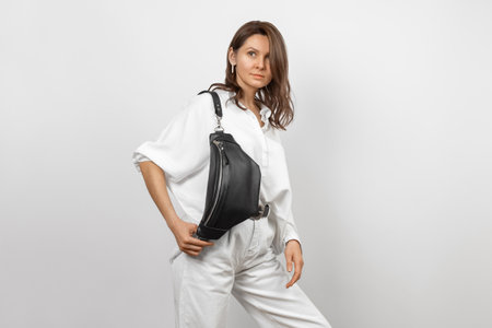 White Woman Wearing White Jeans, Shirt and Crossbody Black Leather Waist Bag over Grey Backgroundの写真素材