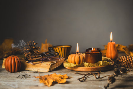 Halloween Still Life on the Wooden Table. Pumpkin Shaped Candles with dry Cones and Leaves, Old Book and Glassesの写真素材
