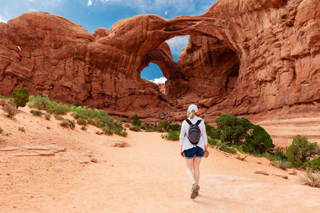 Woman Hiking to the Double Arch Sandstone Rock Formation. The Windows Section Trail with Doble Arch, Natural Wonder in Arches National Park, Utah, United States.の写真素材