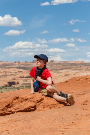 Young Hiker Resting Enjoying the View of Rock Formations in Utah. Boy Sitting while Having a Break in Desert of Arches National Park, United Statesの写真素材