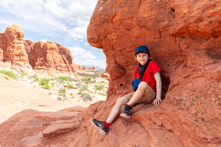 Tourist Boy Sitting on the Red Rock in Arches National Park in Utah. Landscape Photo in the Summerの写真素材
