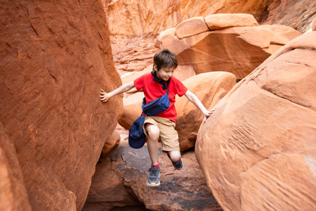 Young Hiker Boy Climbing through the Narrow Path in Sandstone Rock Formation in Arches National Park, Utah, United States.の写真素材