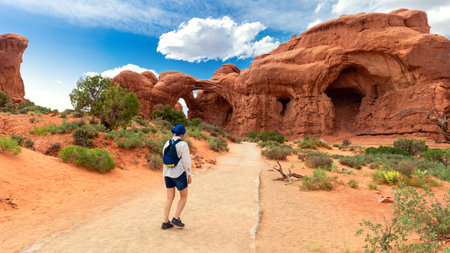Woman Hiking to the Double Arch Sandstone Rock Formation. The Windows Section Trail with Doble Arch, Natural Wonder in Arches National Park, Utah, United States.の写真素材