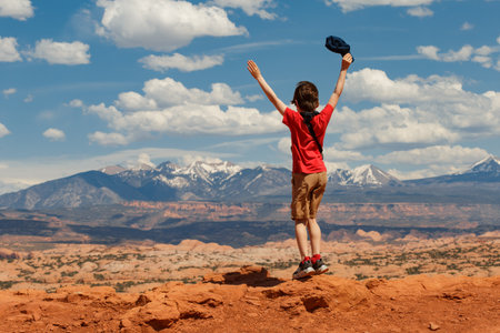 Happy Young Hiker Standing with his Hands up Enjoying the Mountain View in Moab, Utah, United States.の写真素材
