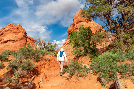 Man Hiking on Mountain Trip in the Windows Section Trail in Arches National Park, Utah, USA. Tourist Wearing White Sun Protective Clothing and Water Backpackの写真素材