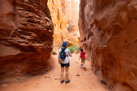 Woman and a Boy Hiking through Narrow Sandstone Desert Rock Canyon Trail in Fiery Furnace, Arches National Park, Utah, United Statesの写真素材