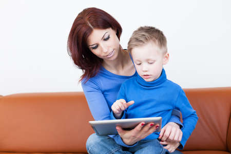 A Mother and her Son sitting on a couch using a Tablet PCの写真素材