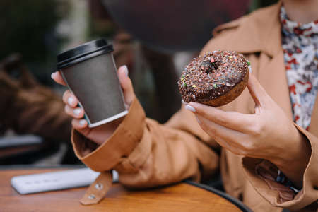 Female hands are holding a donut and a cup of coffeeの写真素材