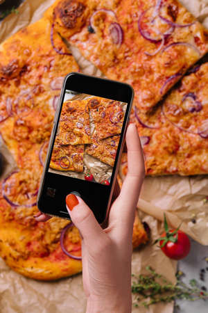 Female hand making a photo of pizza with a mobile phoneの写真素材