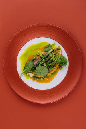 Fish dish - fried cod fillet with asparagus and basil served on red plateの写真素材