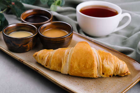 Fresh french croissants with chocolate on plate, blueberry jam, honey, and teaの写真素材