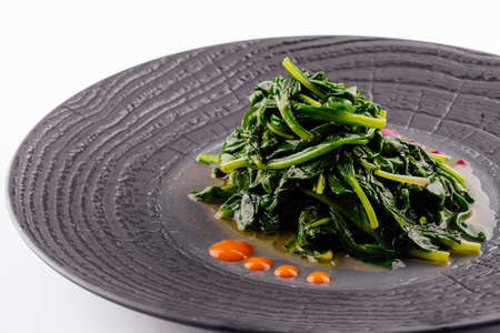 Fried spinach on black plate isolatedの写真素材