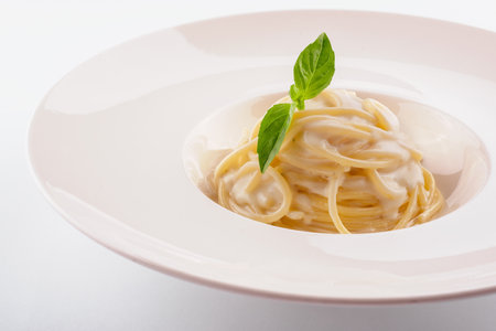 Spaghetti with white cream sauce on white plateの写真素材