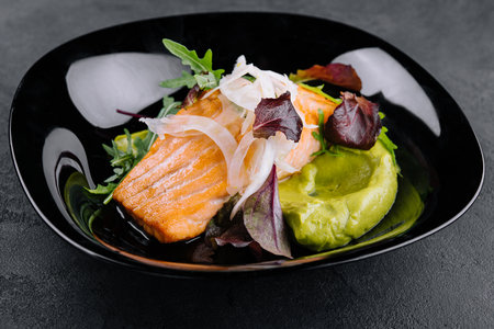 Close-up of grilled salmon fillet with green arugula sprouts with mashed avocado on a plate.の写真素材